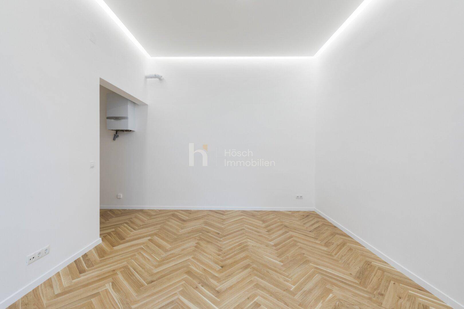 Leerer Raum mit Fischgrätparkett und indirekter Deckenbeleuchtung, ideal für verschiedene Nutzungen.