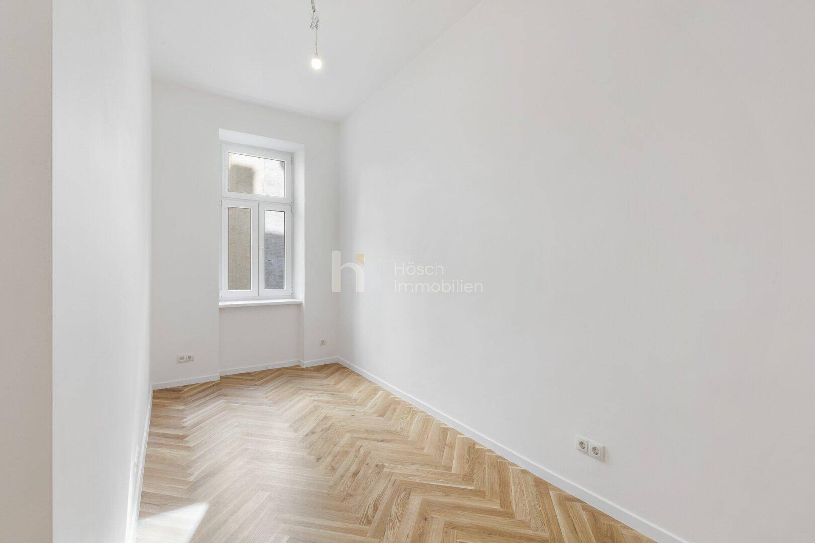 Schmaler Raum mit Fischgrätparkett und einem hohen Fenster, bietet natürliches Licht.