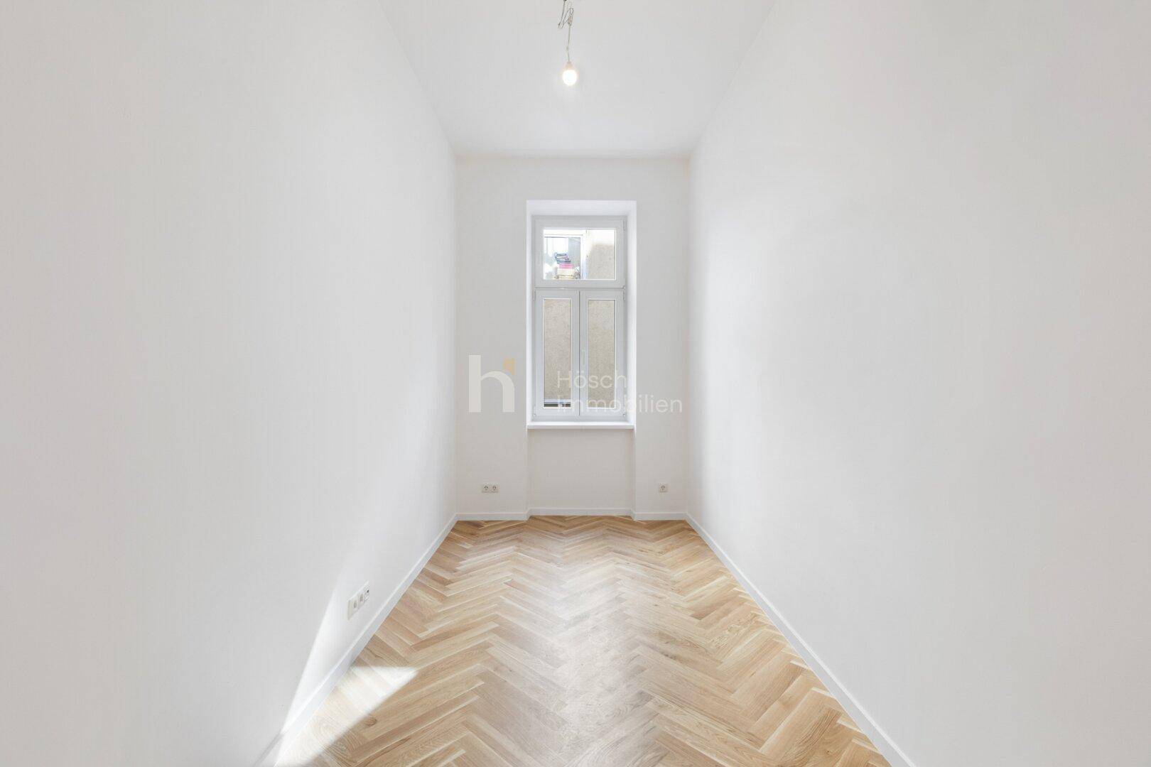 Langer, schmaler Raum mit Fischgrätparkett und einem hohen Fenster, ideal für ein Büro.