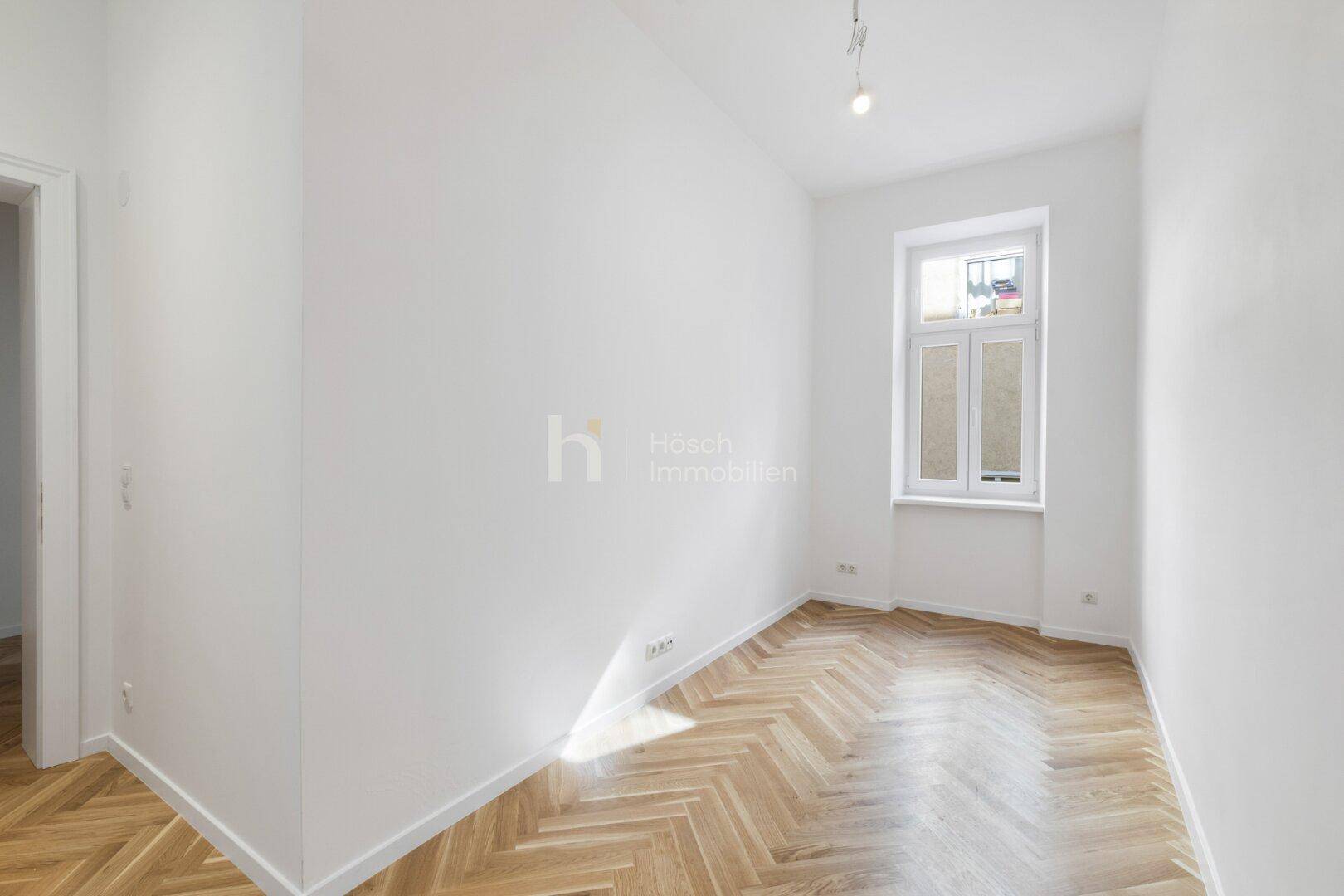 Heller Raum mit Fischgrätparkett und einem hohen Fenster, bereit zur individuellen Einrichtung.