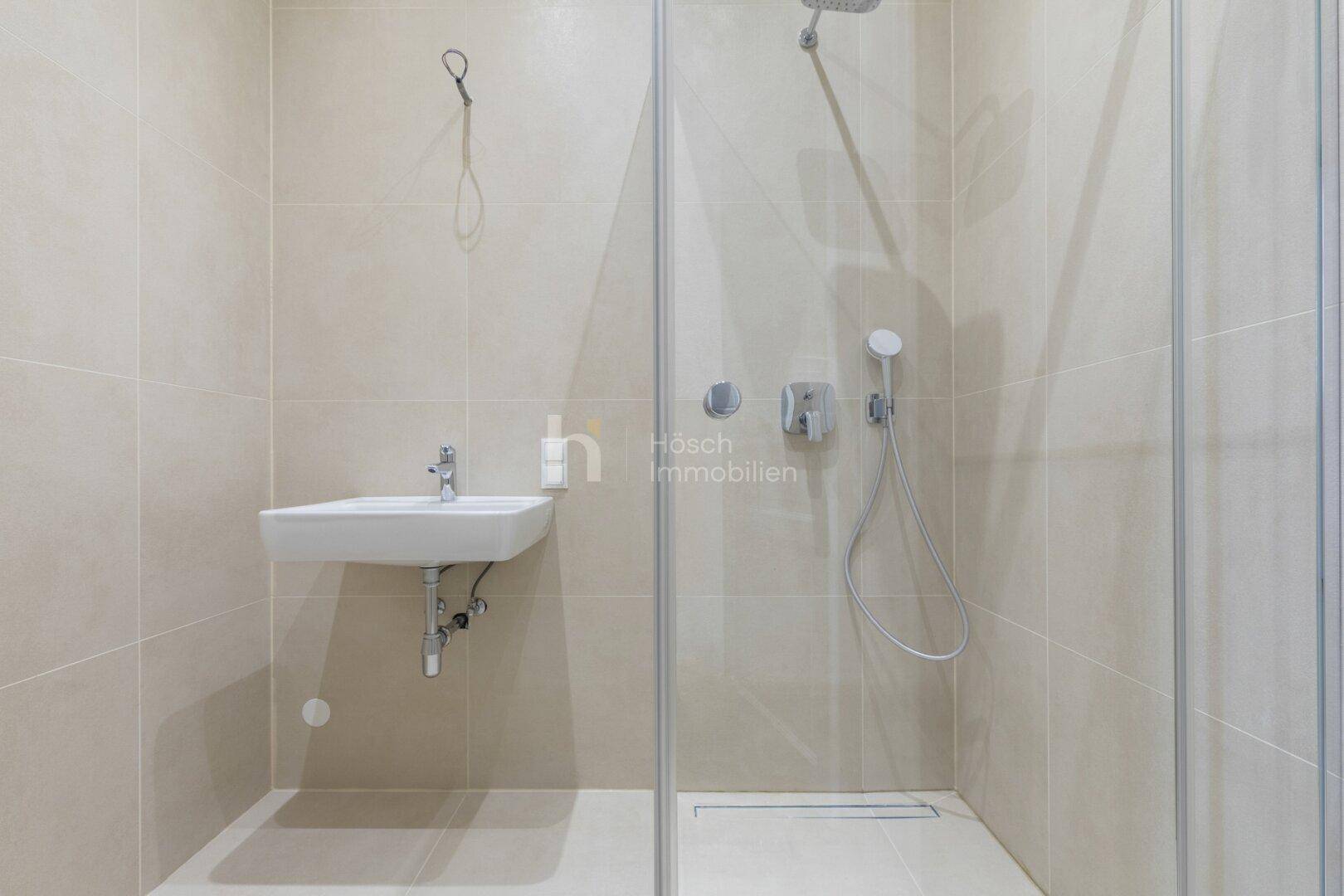 Modernes Badezimmer mit begehbarer Dusche, beigefarbenen Fliesen und minimalistischem Waschbecken.