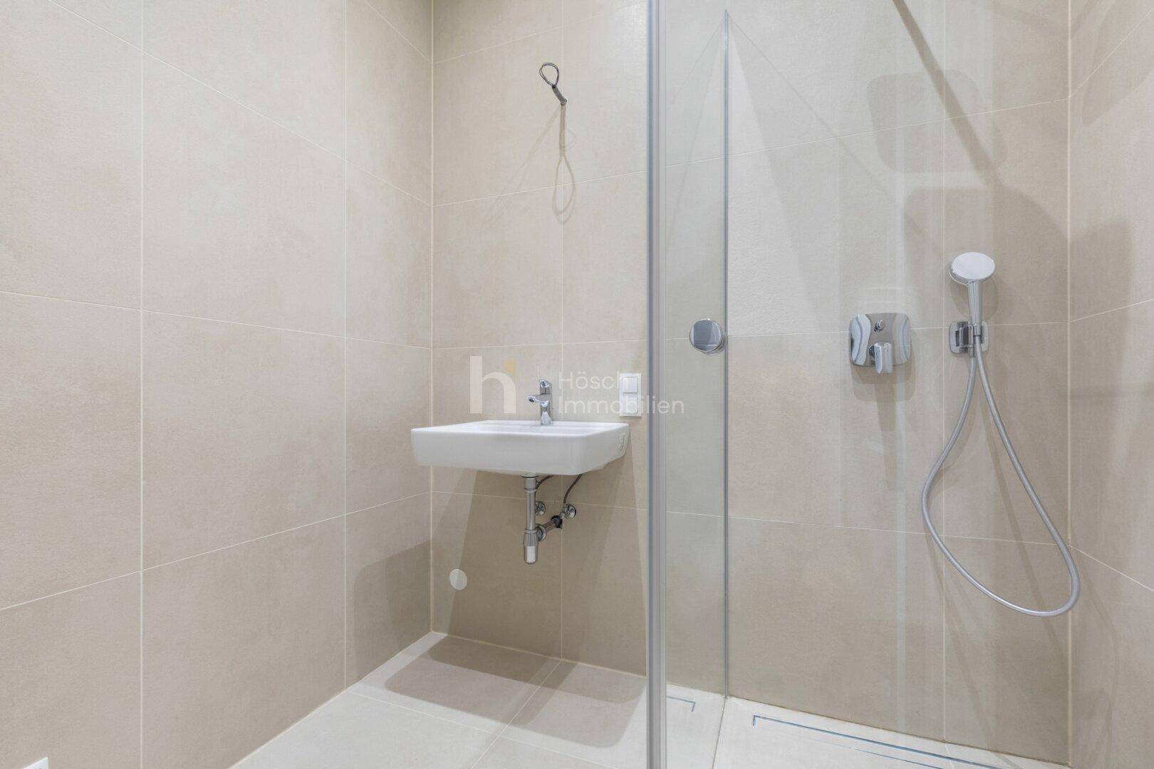 Modernes Badezimmer mit begehbarer Dusche, beigefarbenen Fliesen und minimalistischem Design.