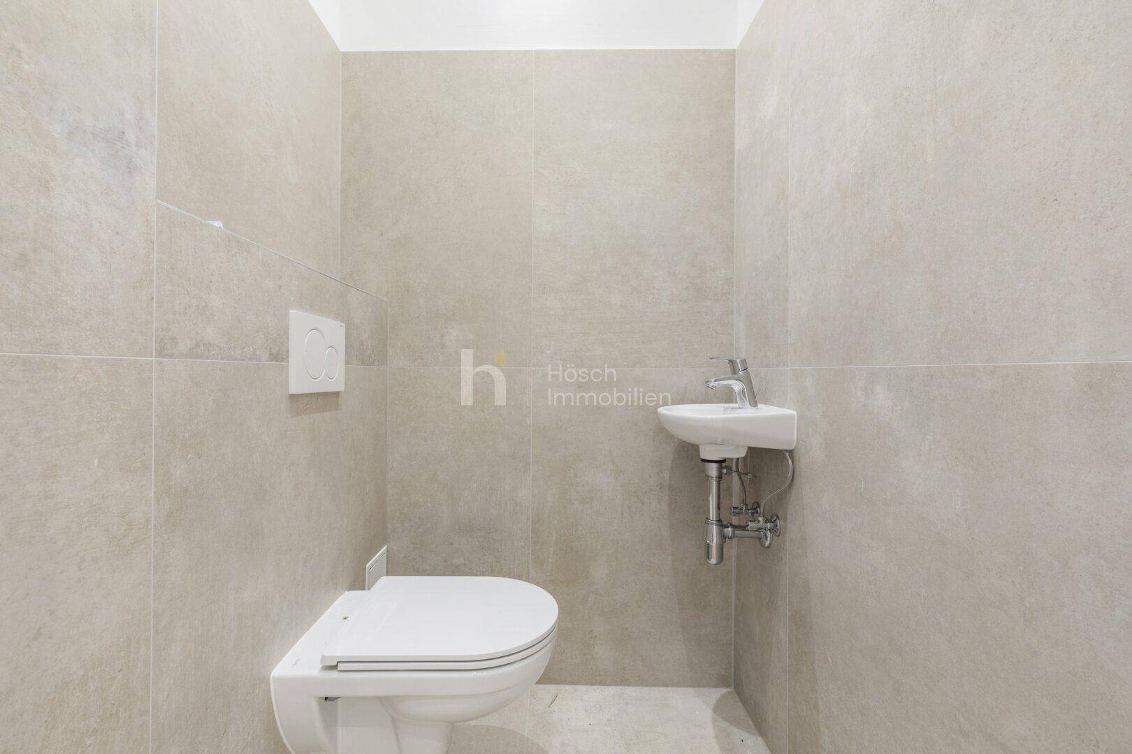 Separates Gäste-WC mit wandhängender Toilette und kleinem Handwaschbecken, komplett gefliest.