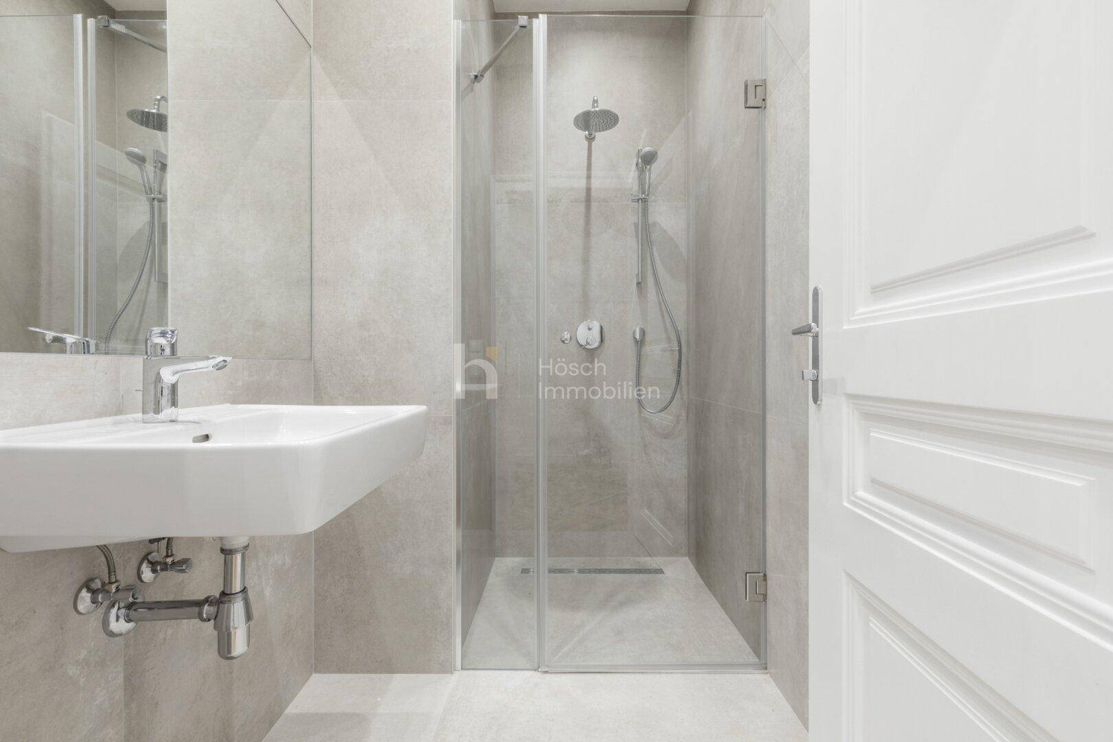 Stilvolles Badezimmer mit grauen Fliesen, modernem Waschbecken und einer großzügigen Glasdusche.