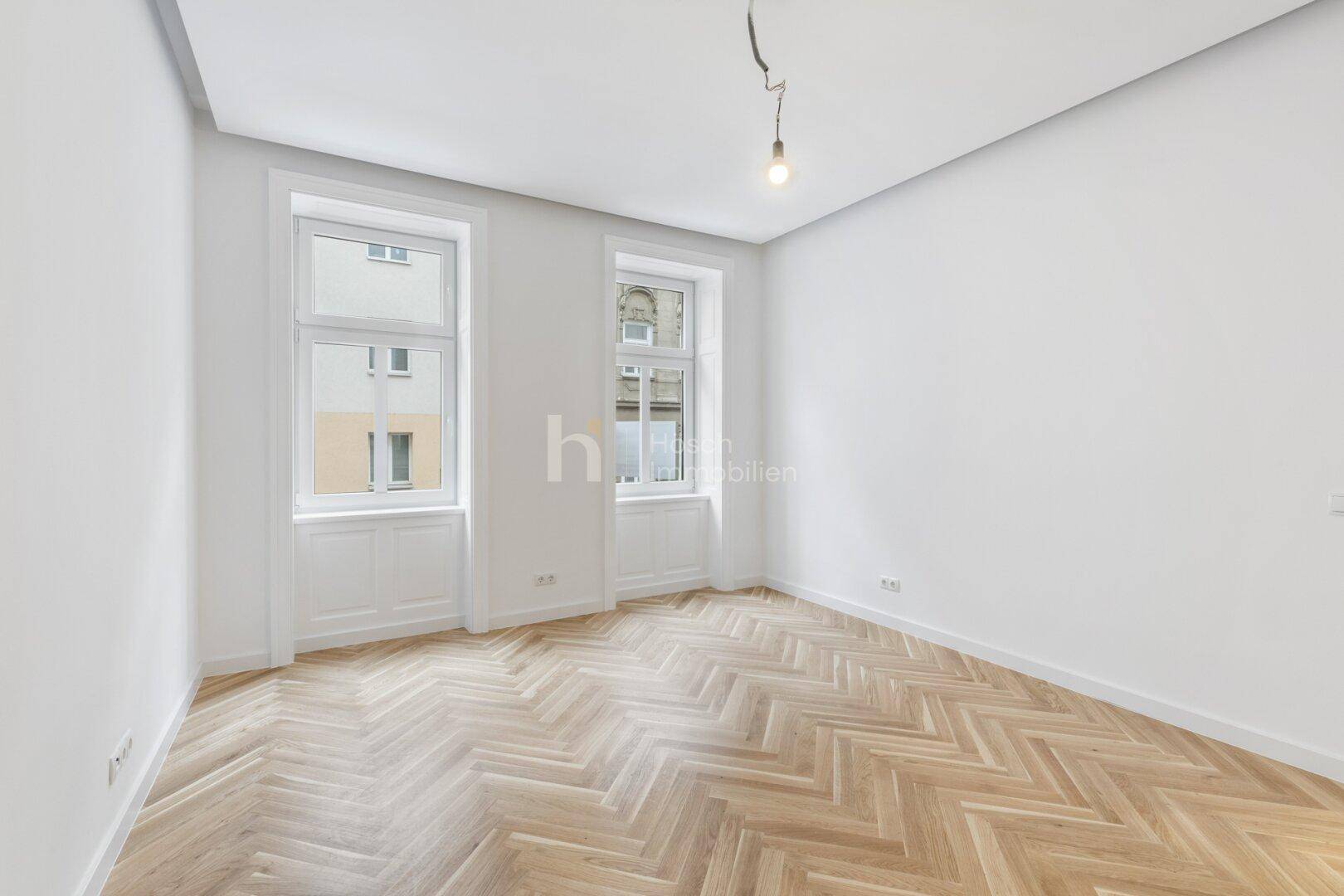 Leerer Raum mit hellem Fischgrätparkett und hohen Fenstern, bereit zur individuellen Gestaltung.