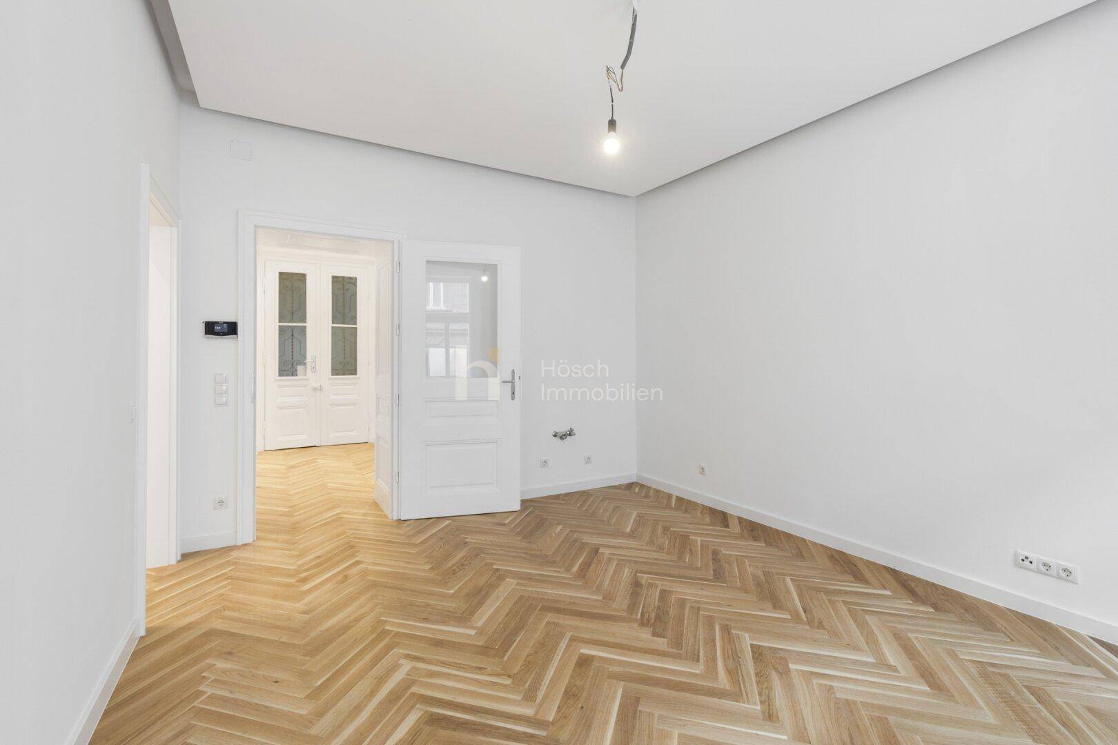 Heller Flur mit Fischgrätparkett und einer Tür, die zu einem weiteren Raum führt.