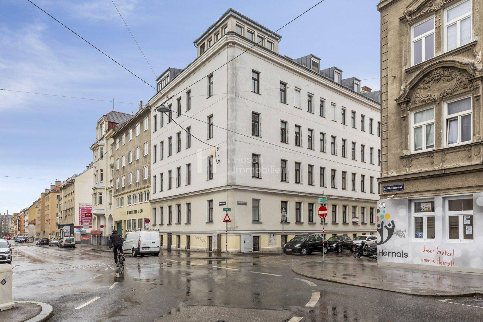 Eckgebäude in urbaner Umgebung mit traditioneller Architektur und Mansarddach, umgeben von Stadtleben.