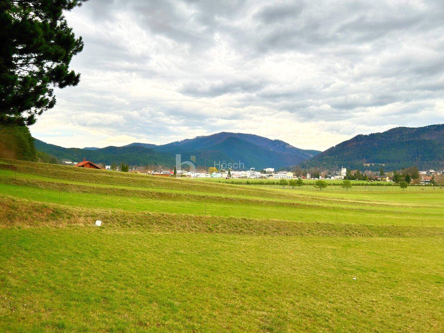 Gestufte grüne Felder mit Blick auf ein entferntes Dorf und Berge unter einem bewölkten Himmel.