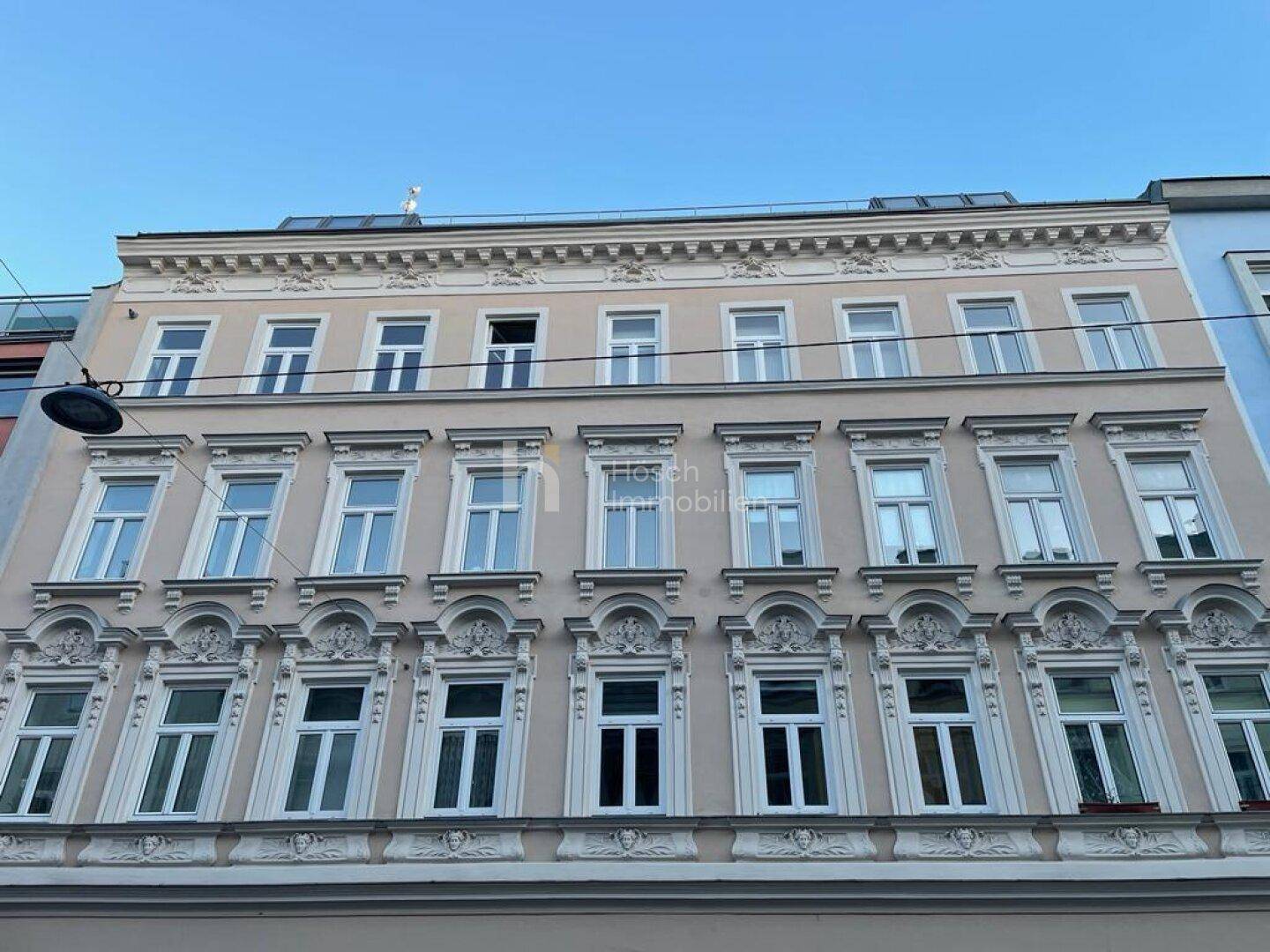 Historische Fassade eines Mehrfamilienhauses mit reich verzierten Fenstern und Stuckelementen.