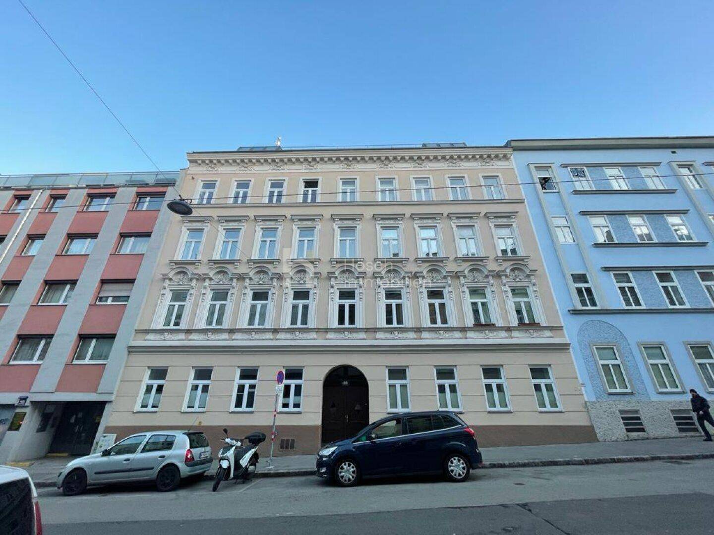 Gesamtansicht der historischen Fassade eines Mehrfamilienhauses an einer Stadtstraße mit parkenden Autos.