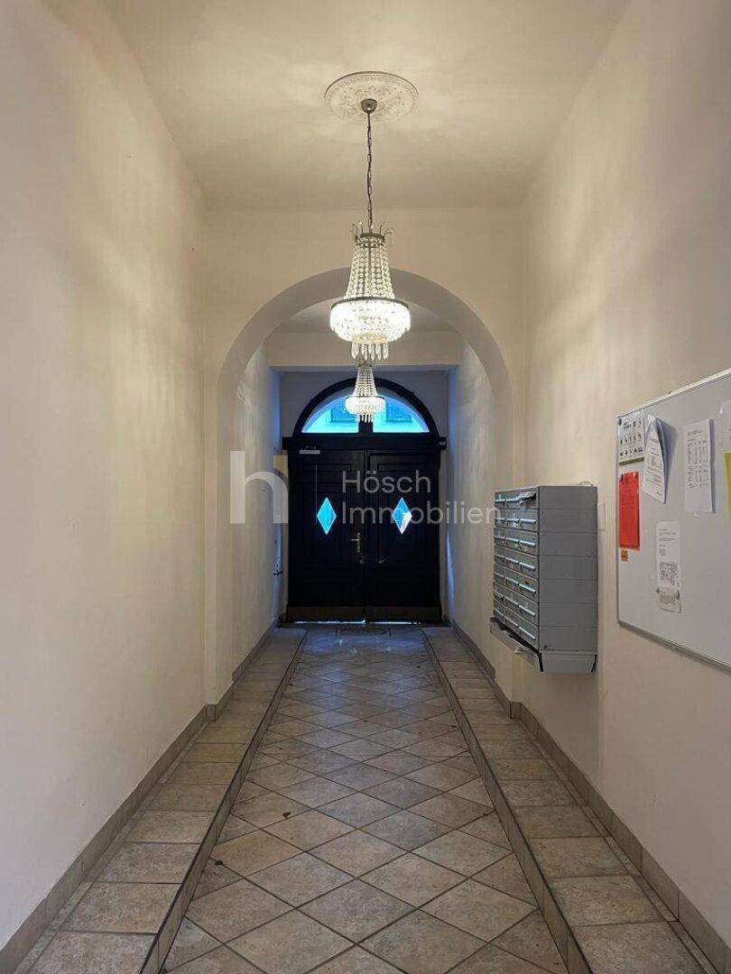 Eingangsbereich mit eleganten Kronleuchtern und gefliestem Boden in einem Altbau mit hohen Decken.