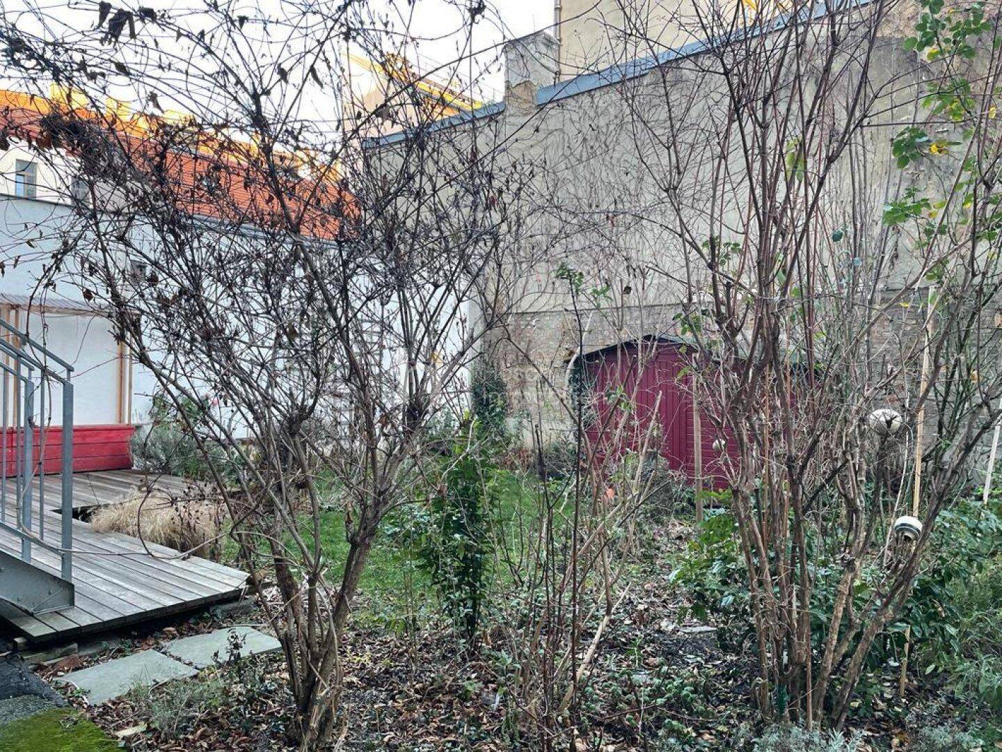 Hinterhofgarten mit Bäumen, Sträuchern und einem kleinen roten Gartenschuppen im Herbst.