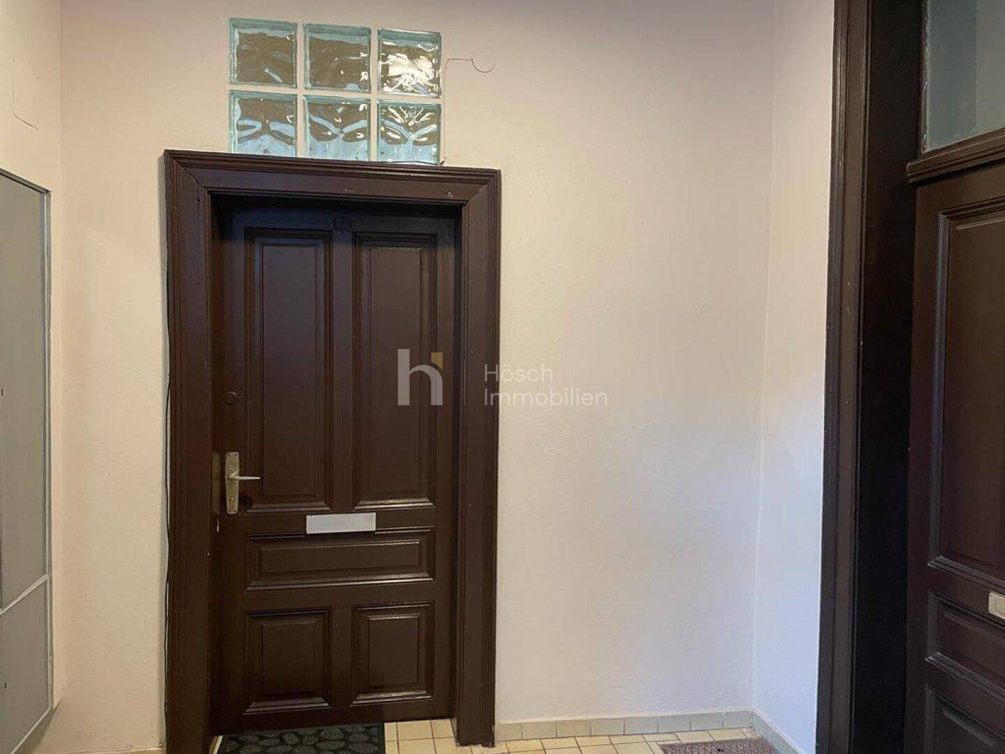 Eingangstür einer Wohnung mit dunklem Holz und Glasbausteinen im oberen Bereich des Flurs.