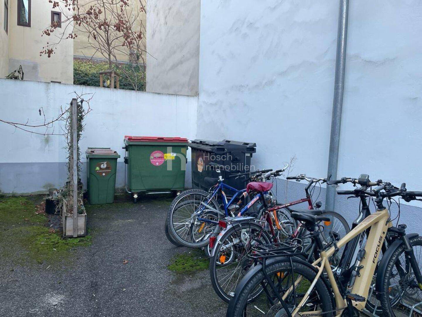 Außenbereich mit Fahrradabstellplätzen und Mülltonnen hinter dem Gebäude im Innenhof.