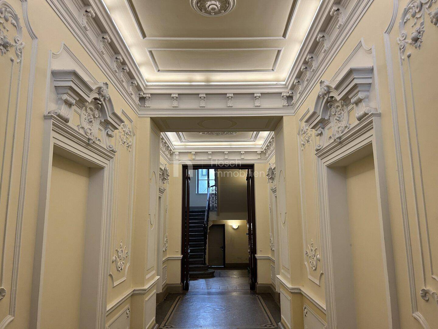 Historischer Flur mit kunstvollen Stuckelementen und hohen Decken, der zum Treppenhaus führt.