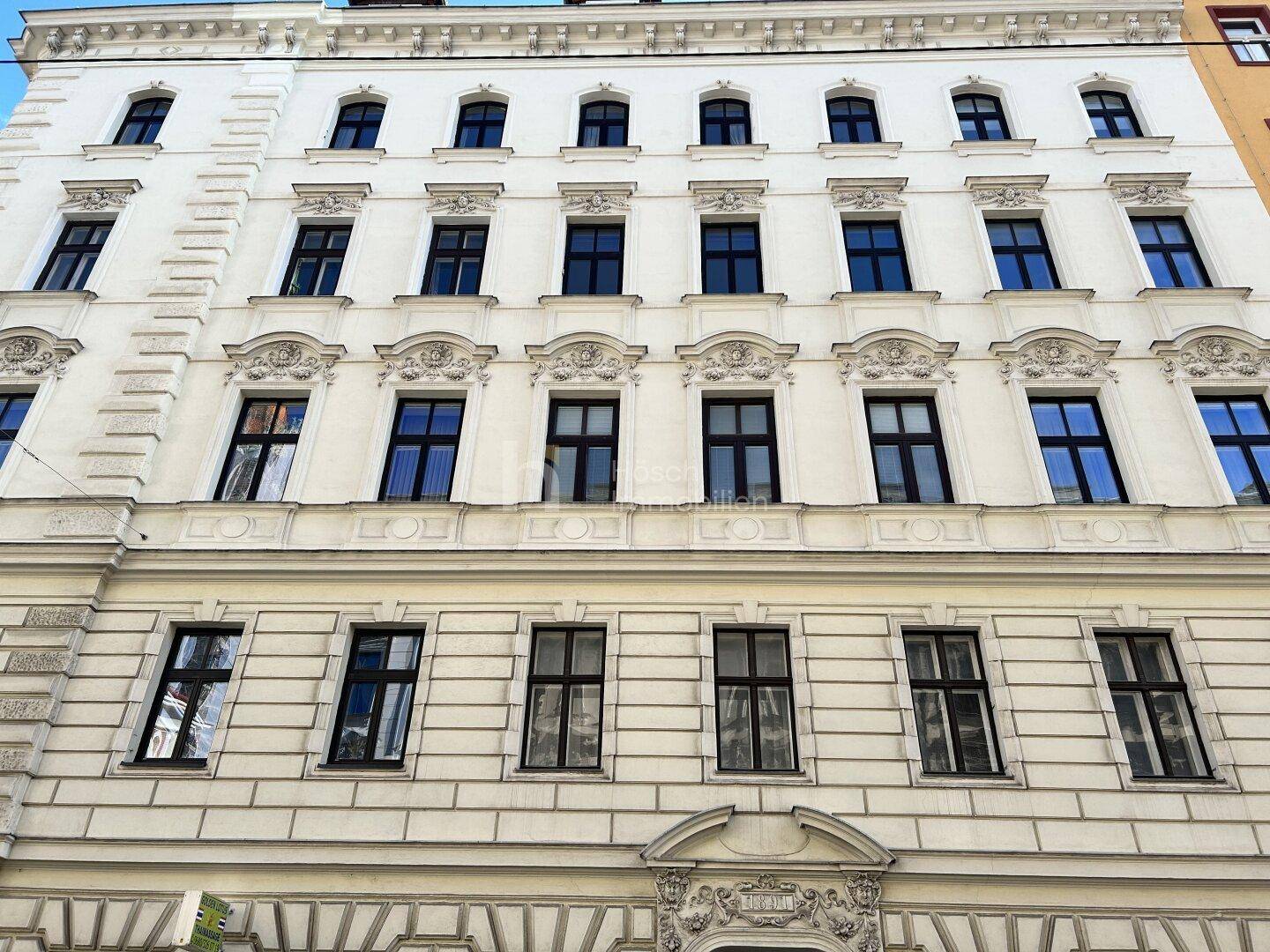 Ansicht der eleganten Fassade eines historischen Wohngebäudes mit vielen Fenstern und Stuckverzierungen.