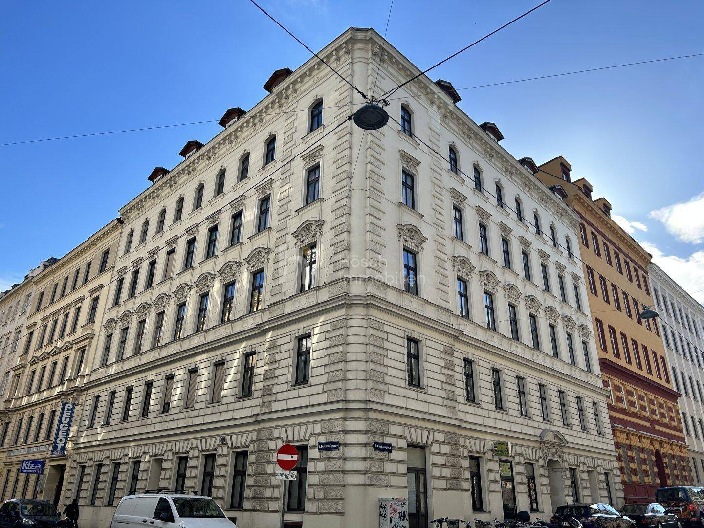 Majestätisches Eckgebäude im Altbaustil mit zahlreichen Fenstern und klassischer Architektur unter blauem Himmel.