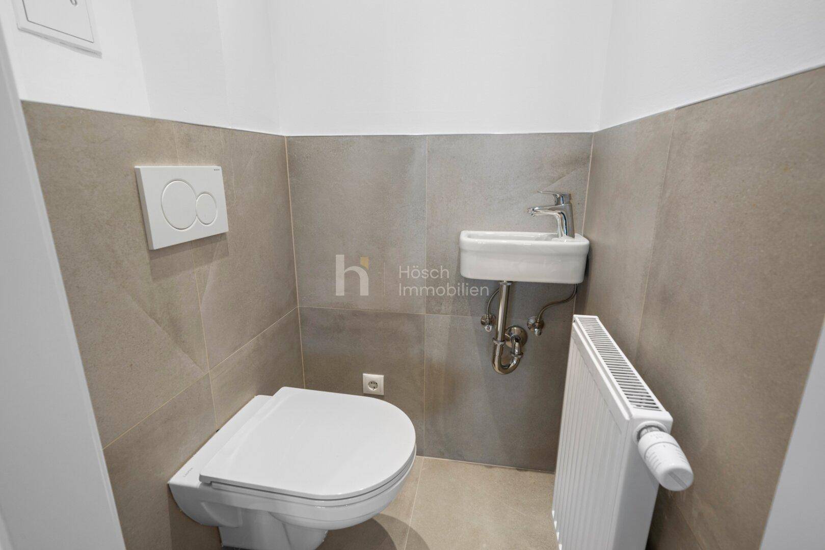 Funktionale Gästetoilette mit wandhängendem WC, kleinem Waschbecken und modernen Fliesen.