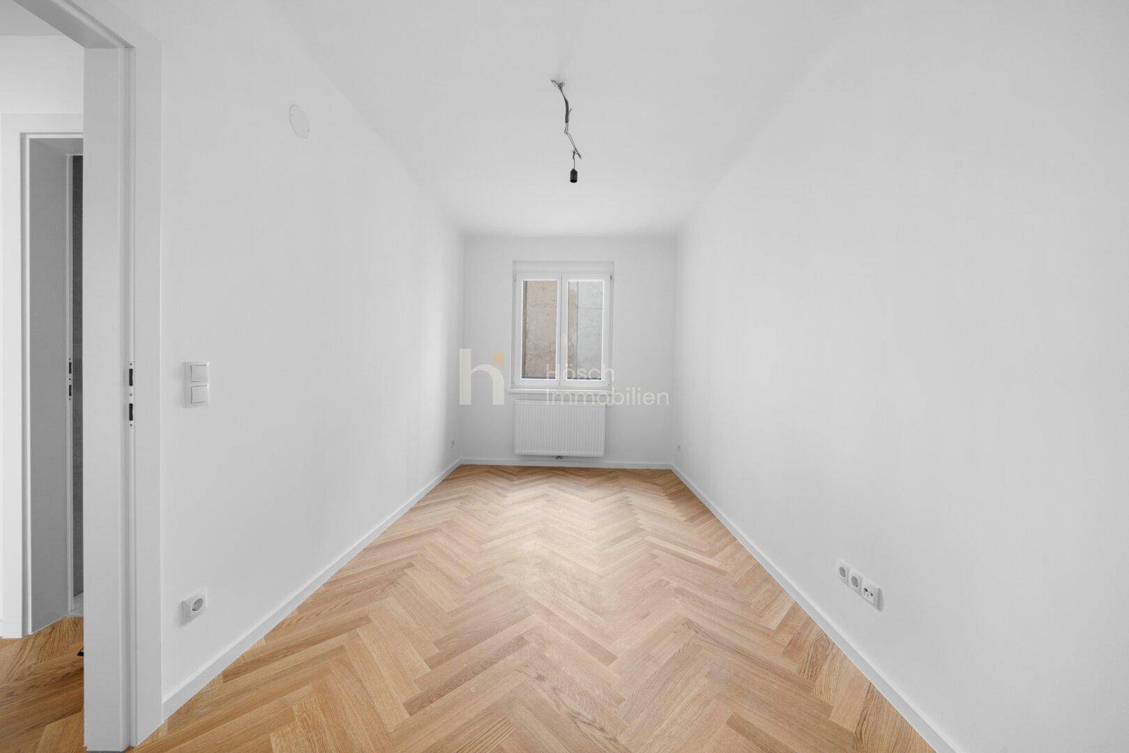 Kleineres, helles Zimmer mit Fischgrätparkett und Fenster, ideal als Kinderzimmer oder Büro.
