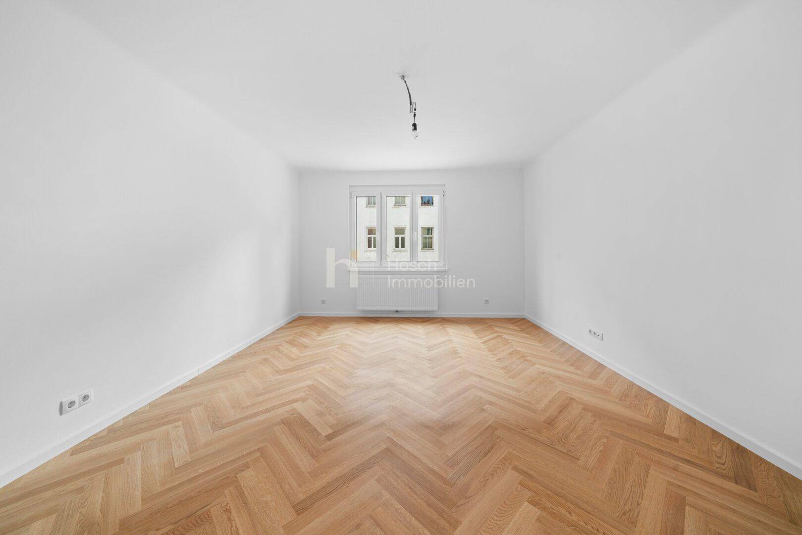 Geräumiges, leeres Zimmer mit Fischgrätparkett und großen Fenstern, bereit zur individuellen Einrichtung.