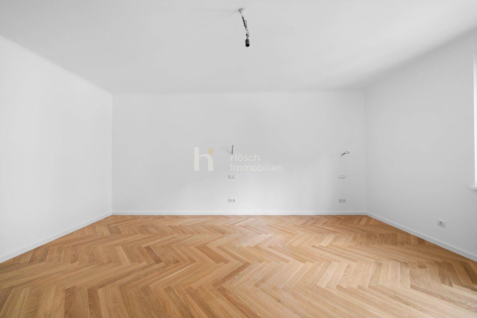 Helles, leeres Schlafzimmer mit Fischgrätparkett und viel Tageslicht, ideal für individuelle Gestaltung.