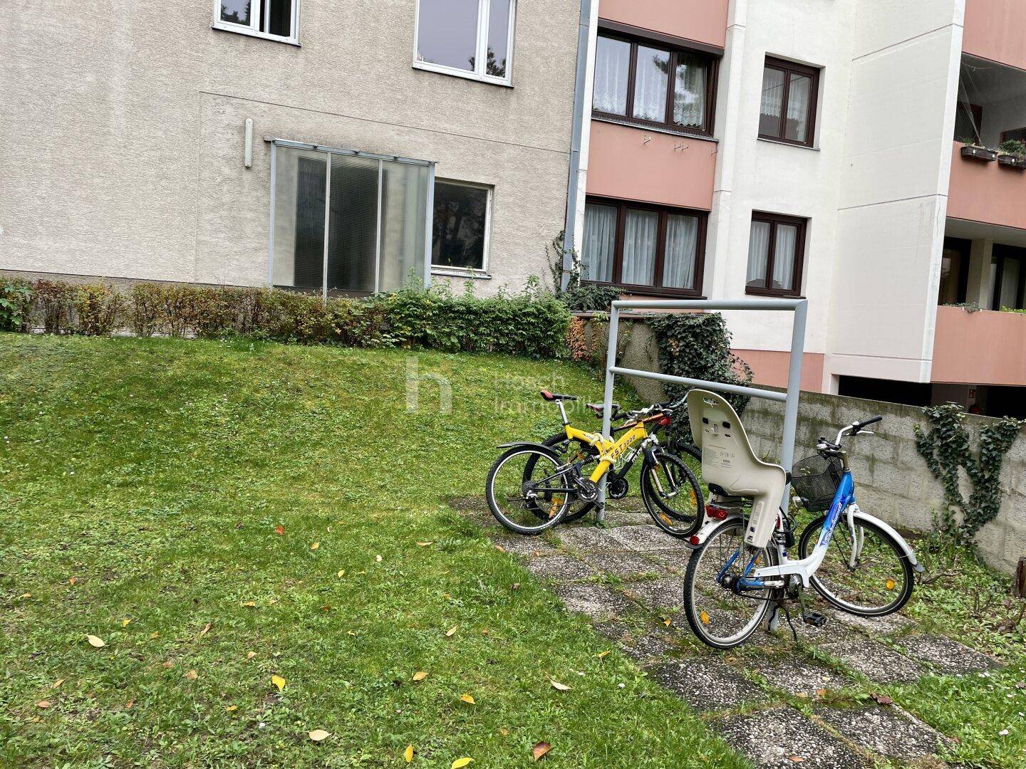 Außenbereich mit Fahrrädern neben dem Gebäude und Grünfläche.