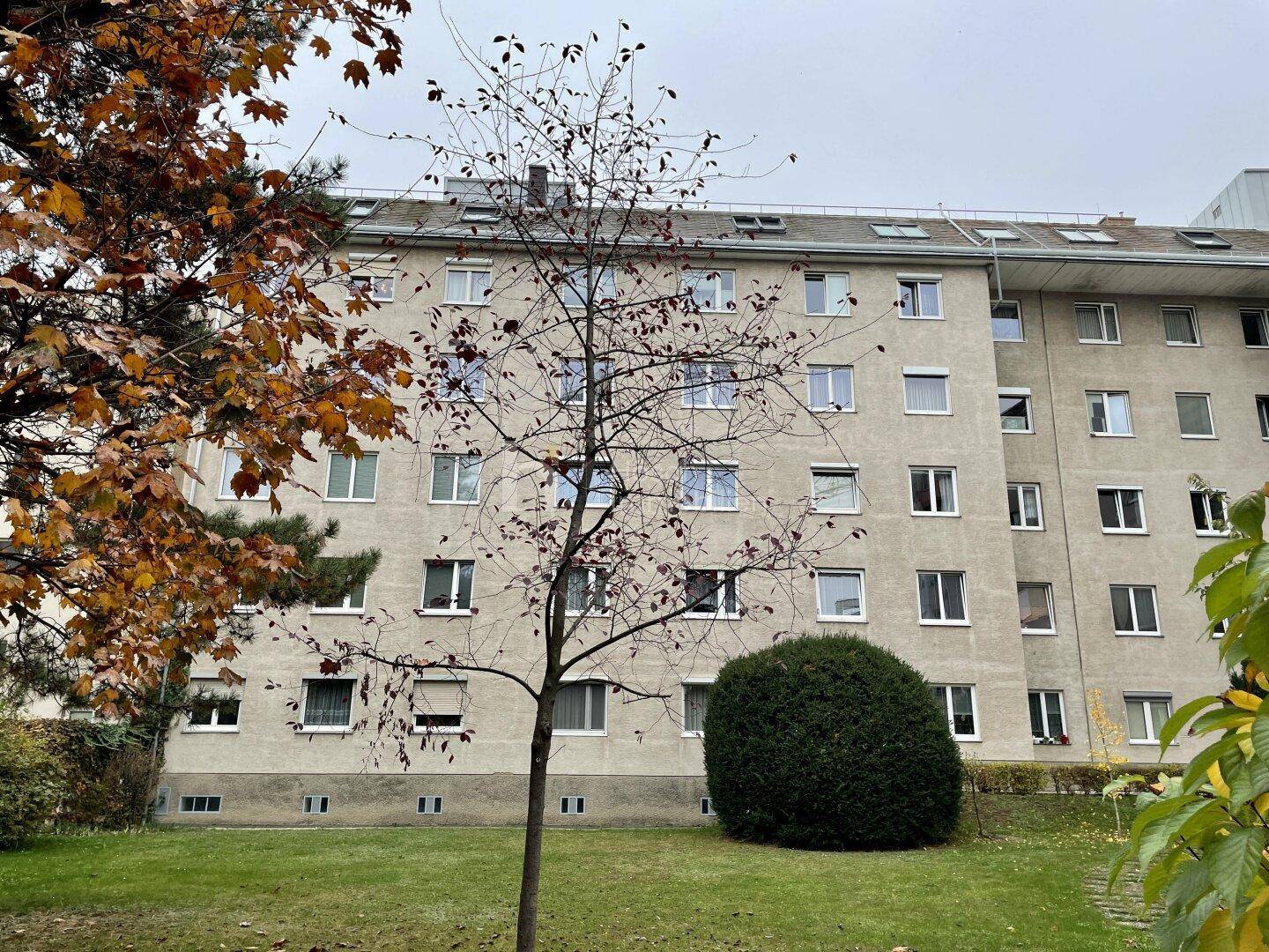 Fassade eines Mehrfamilienhauses mit vielen Fenstern und umgebendem Grün.