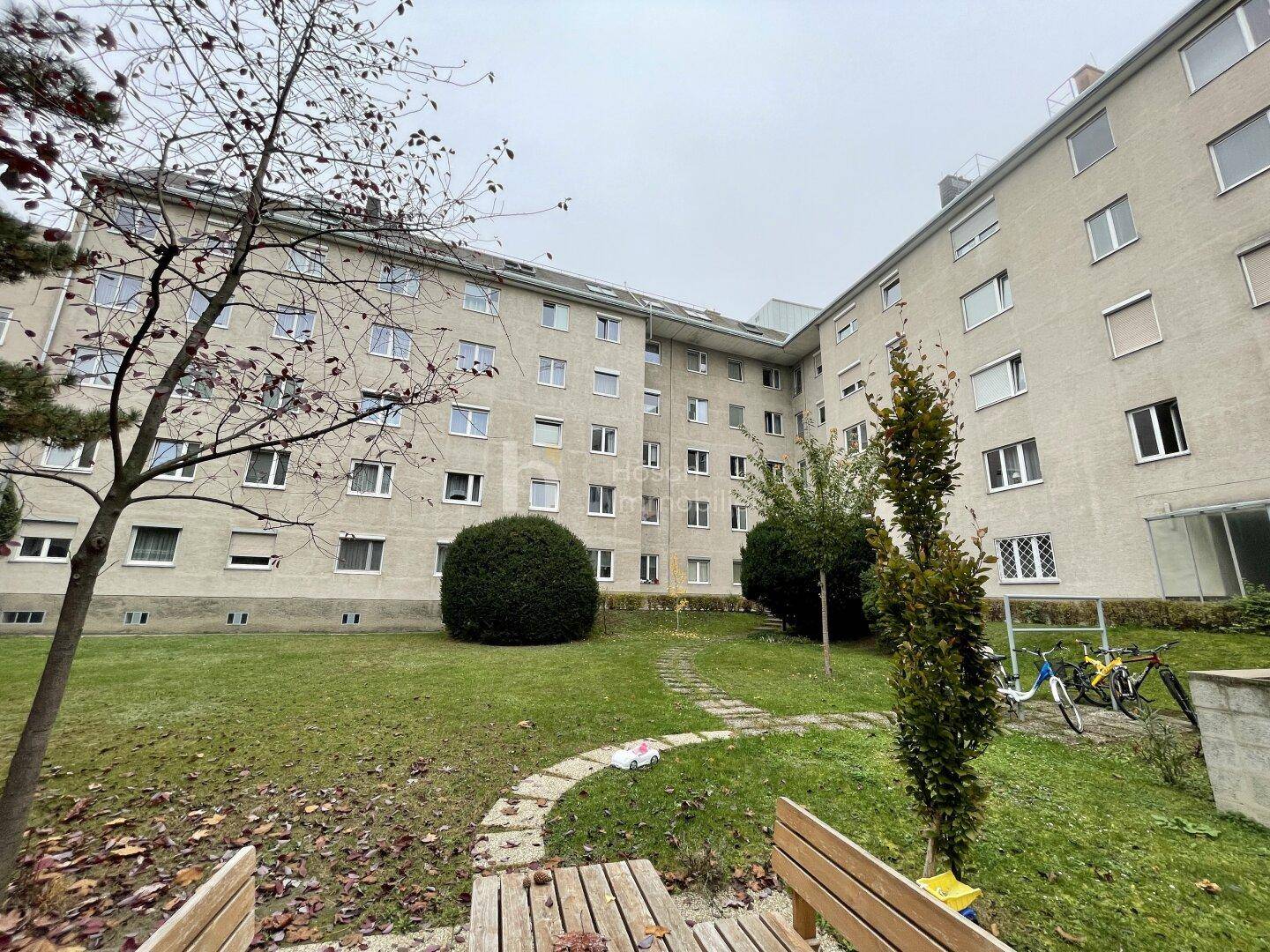 Weitläufiger Gemeinschaftsgarten mit Sitzbank und Blick auf die Gebäudefassade.