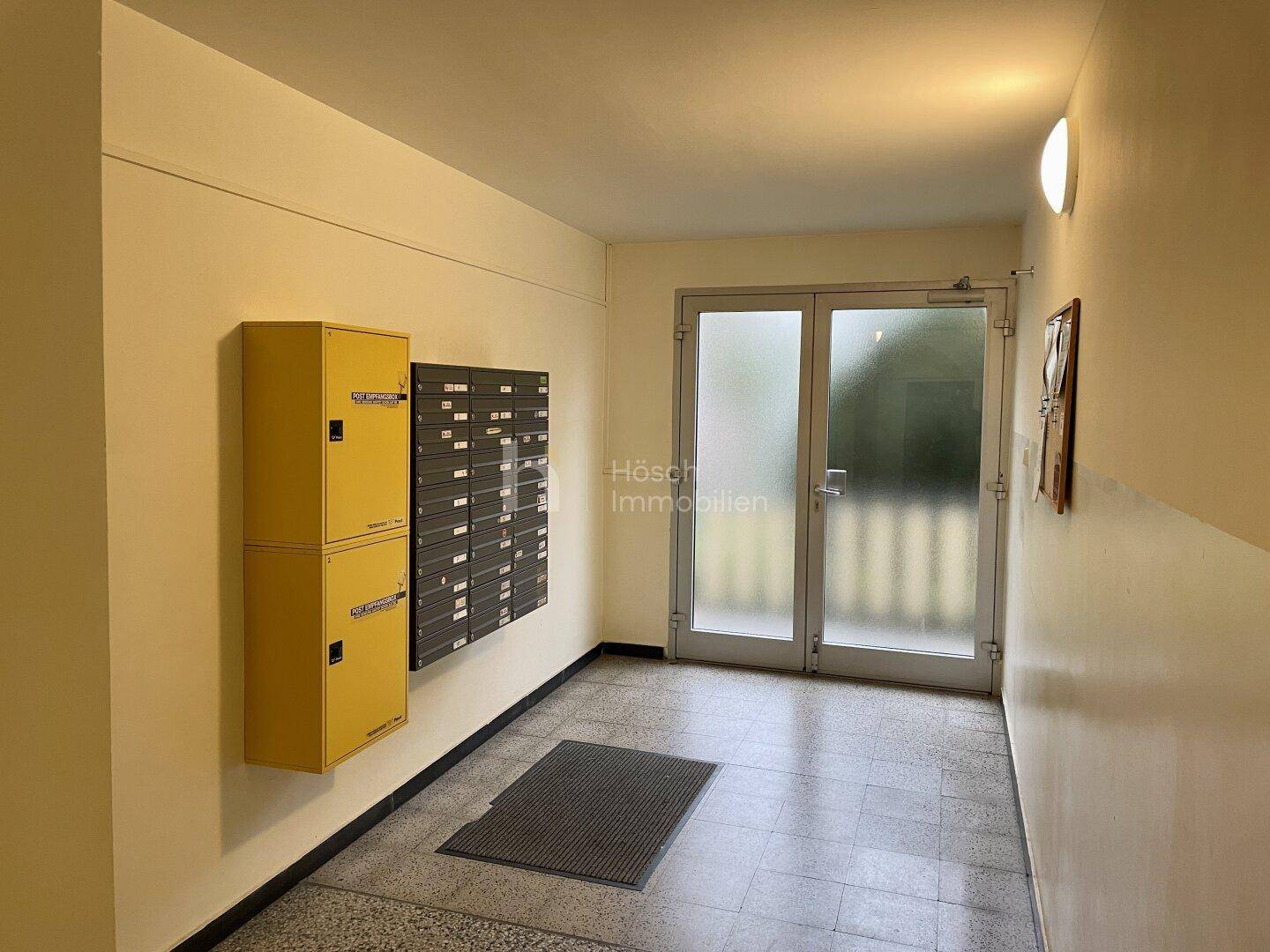 Eingangsbereich des Gebäudes mit Briefkästen und Glastüren, hell und einladend.