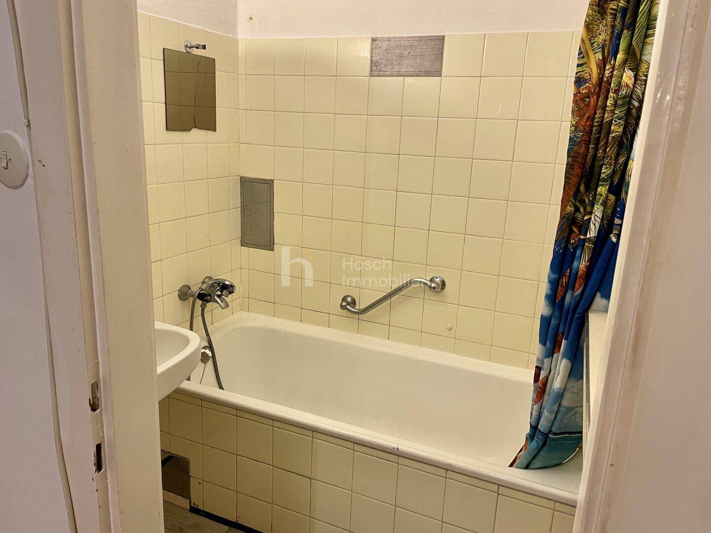 Badezimmer mit Badewanne, Waschbecken und hellen Fliesen, im Stil der 80er Jahre.