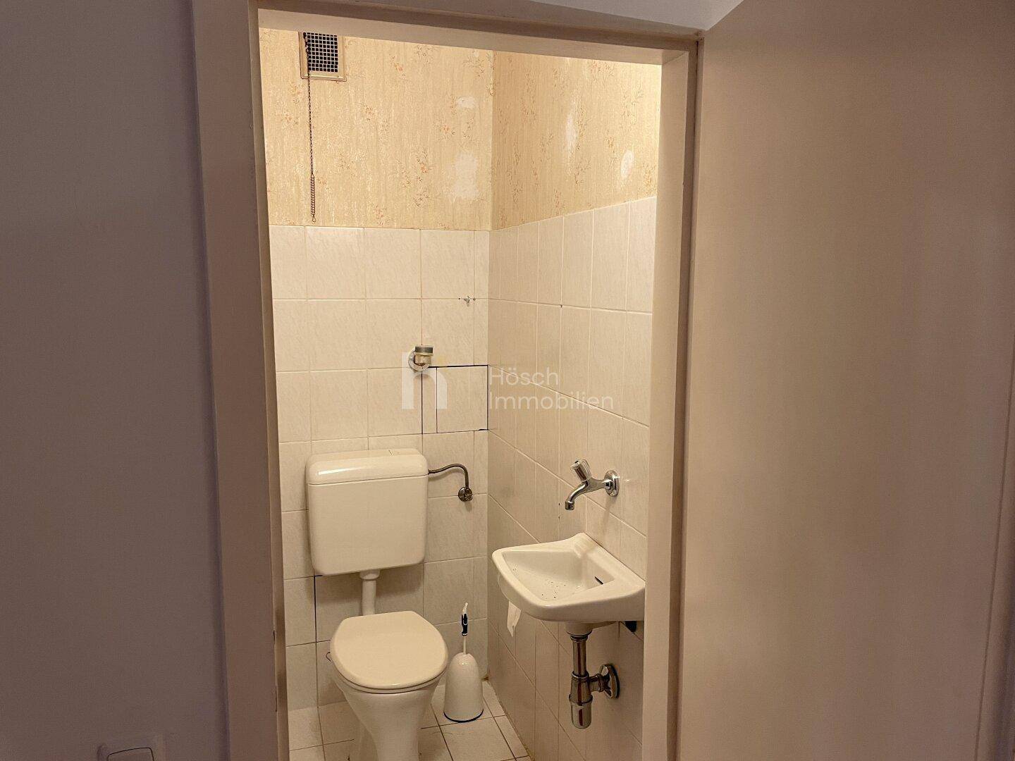 Kleines Gäste-WC mit Toilette und Handwaschbecken, einfach ausgestattet.