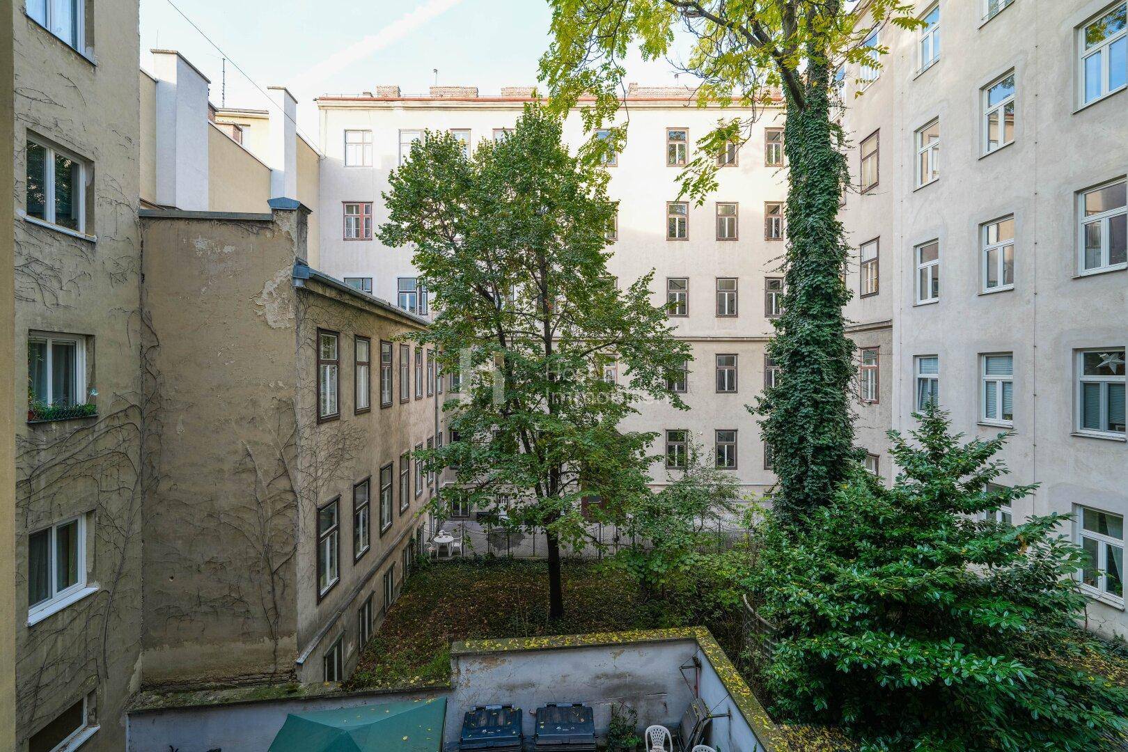 Grüner Innenhof mit Bäumen und Sträuchern, umgeben von Wohngebäuden.