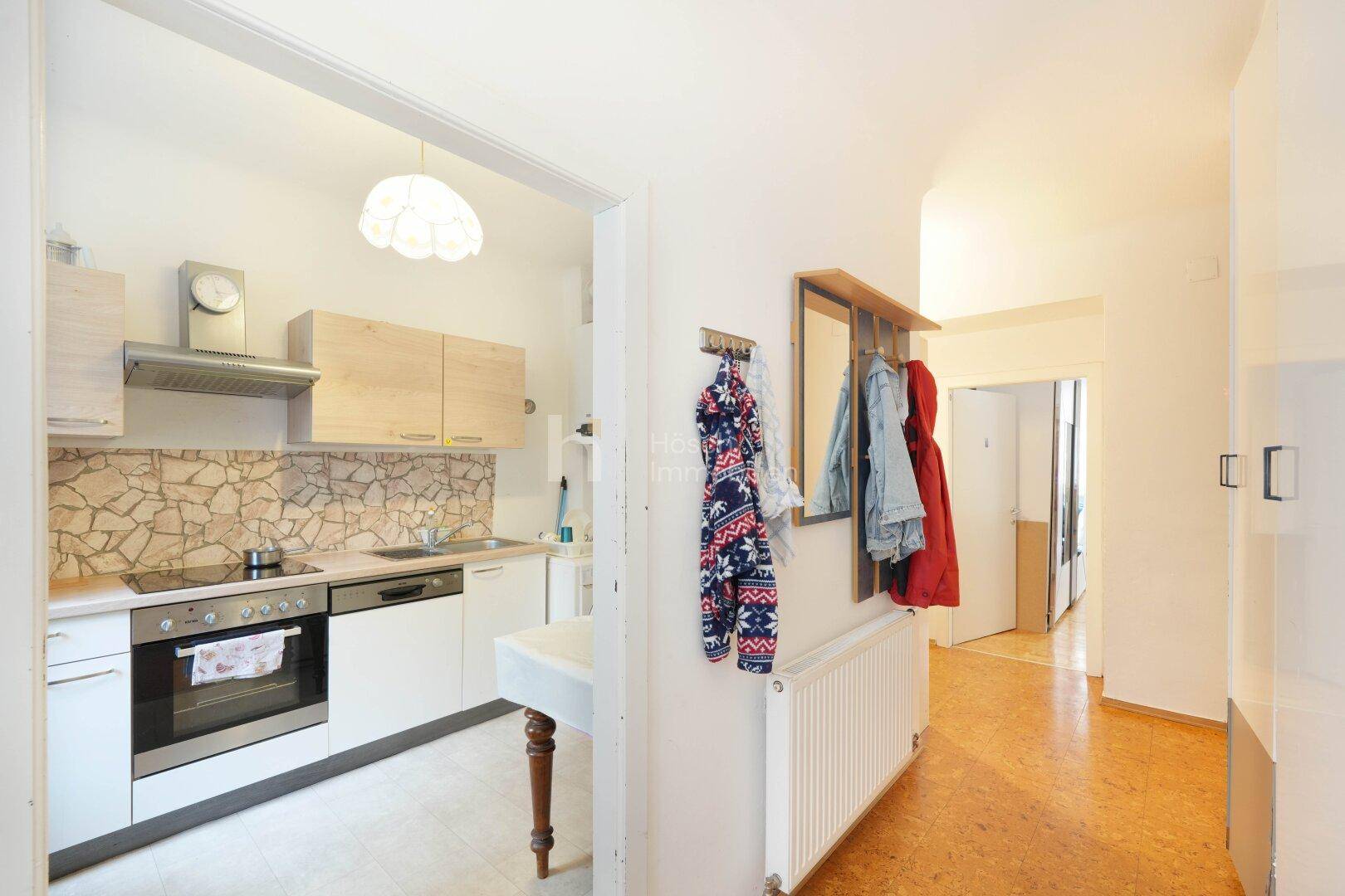Heller Flur mit Garderobe und Blick in die angrenzende Küche mit Steinrückwand.