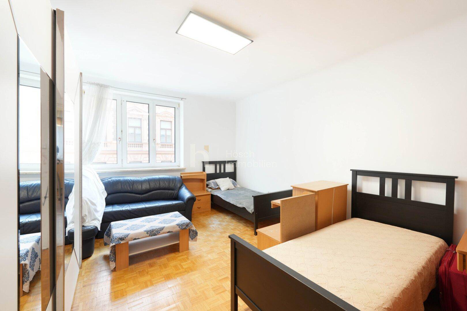 Helles Schlafzimmer mit zwei Einzelbetten, Sofa, Kleiderschrank und Parkettboden.