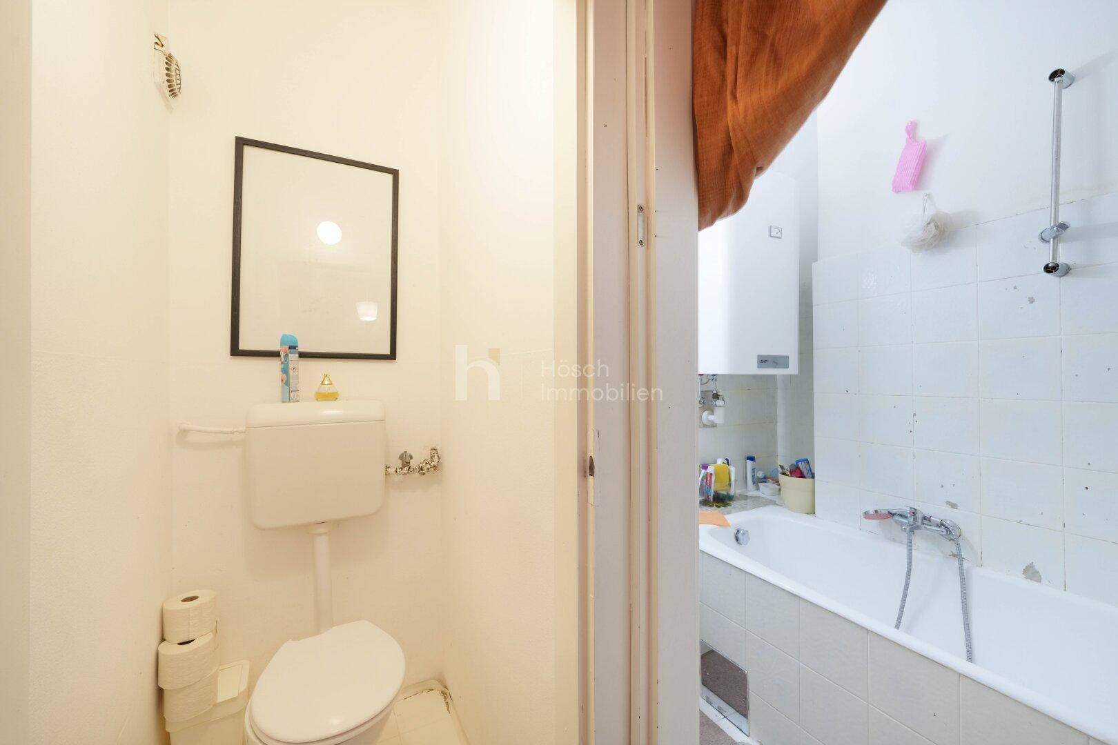 Separate Toilette mit WC, Spülkasten und Blick in das angrenzende Badezimmer.