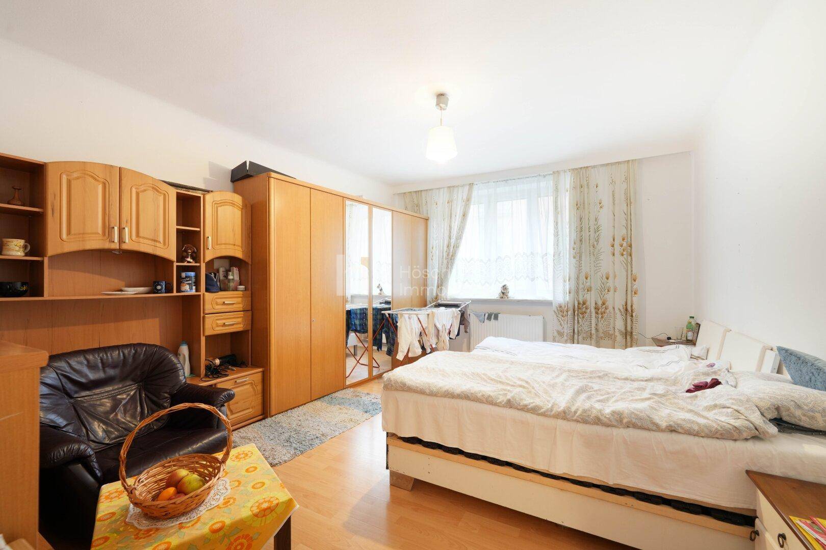 Schlafzimmer mit Holzmöbeln, Doppelbett, Kleiderschrank und Fenster mit Vorhängen.