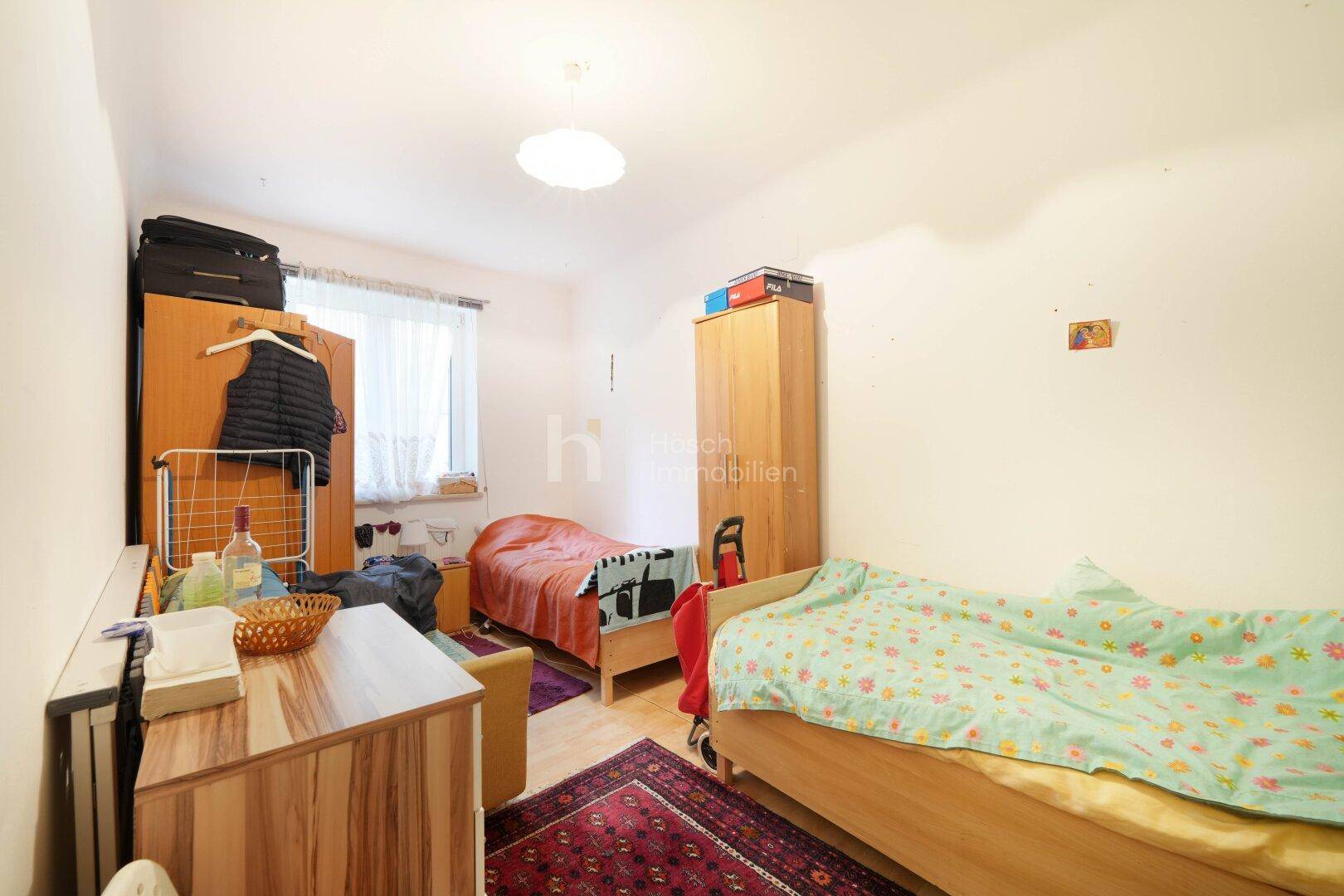 Schlafzimmer mit zwei Einzelbetten, Holzmöbeln und Fenster mit Blick ins Grüne.