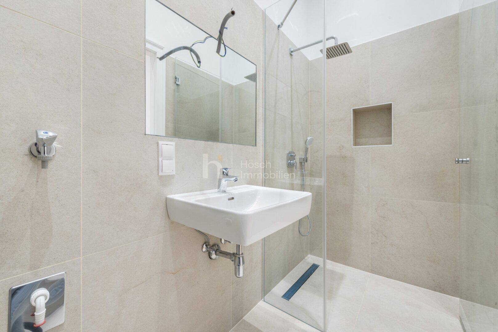 Modernes Badezimmer mit ebenerdiger Dusche, Einzelwaschbecken und hellen, großformatigen Fliesen.