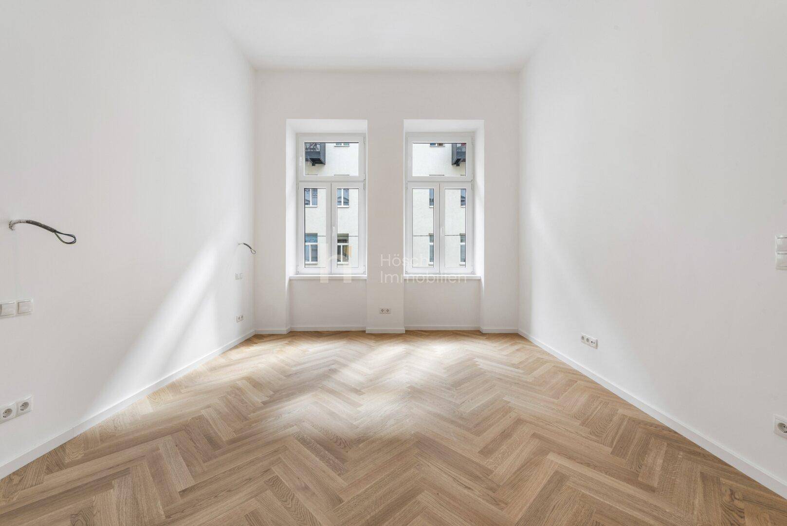 Geräumiges Zimmer mit Fischgrätparkett und zwei großen Fenstern, ideal für individuelle Gestaltung.