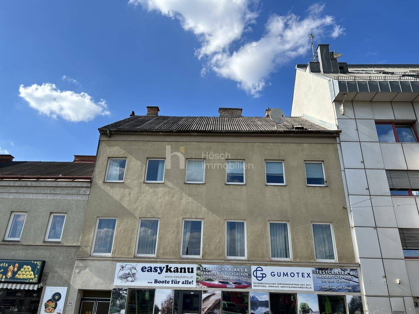 Fassade eines älteren Gebäudes mit mehreren Fenstern und Geschäftsflächen im Erdgeschoss.