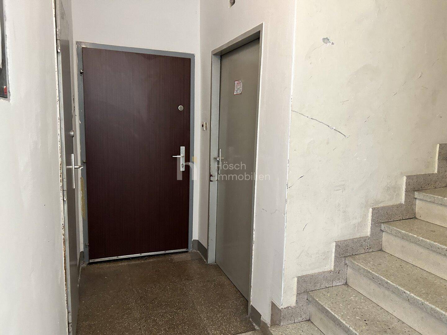 Treppenhausbereich mit zwei Wohnungstüren und einer Steintreppe, die nach oben führt.