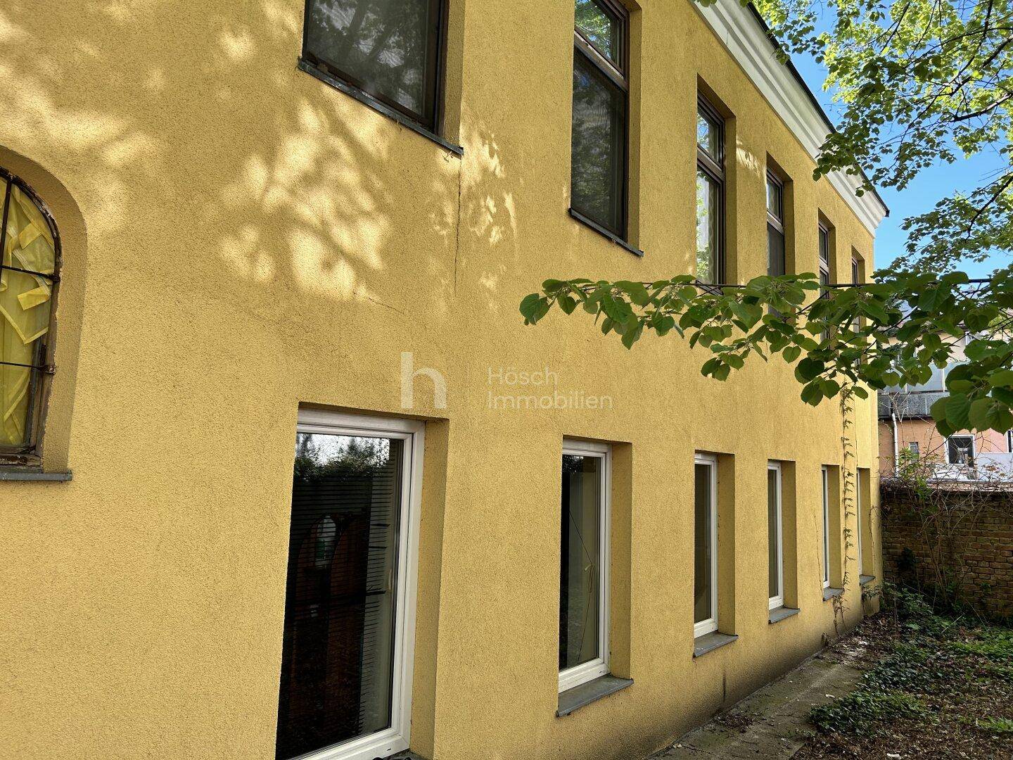 Seitenansicht des gelben Gebäudes mit mehreren Fenstern und Blick auf den ungepflegten Garten.