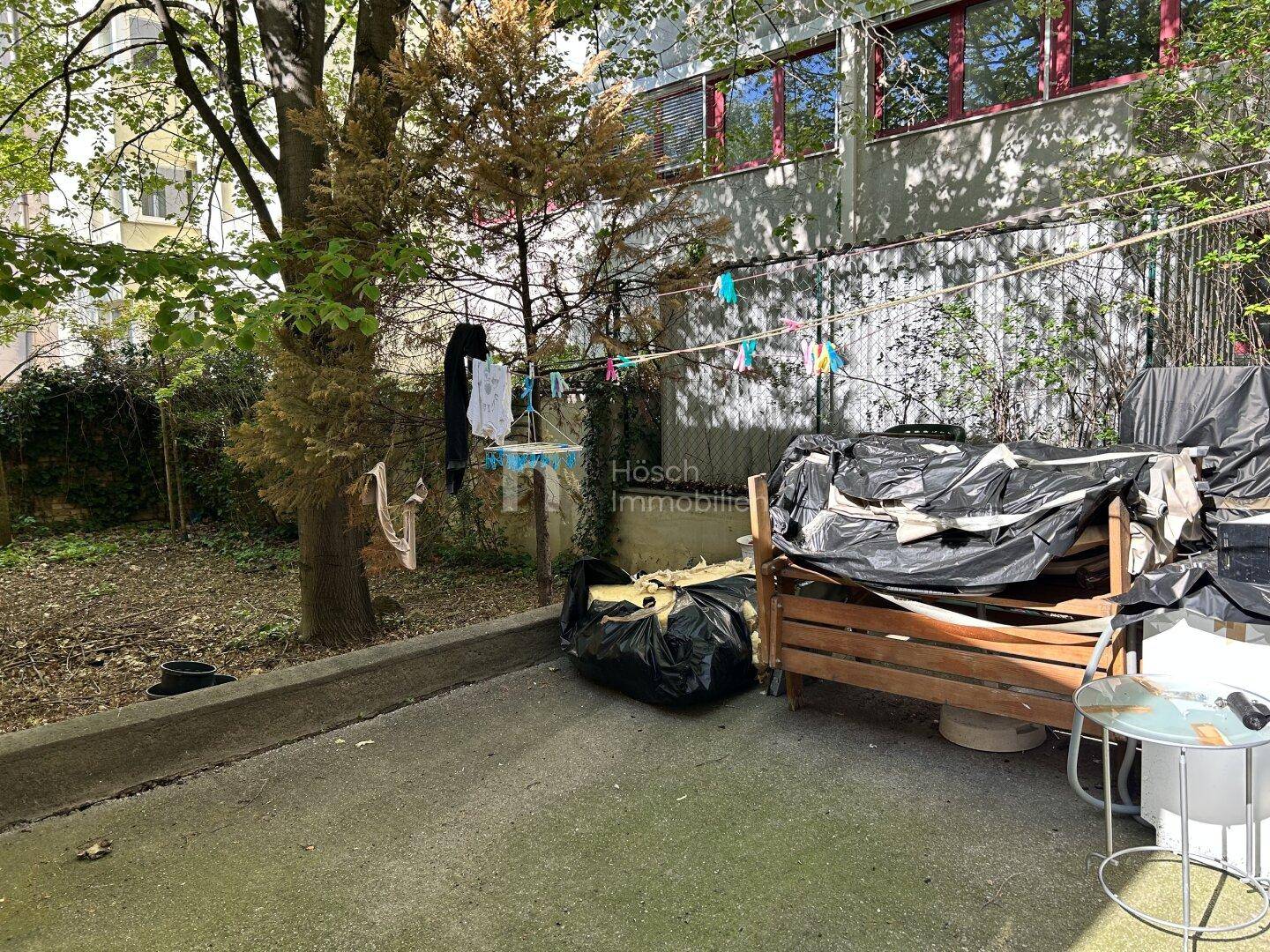 Hinterhofbereich mit gepflastertem Boden, Wäscheleine und verschiedenen Gegenständen im Freien.