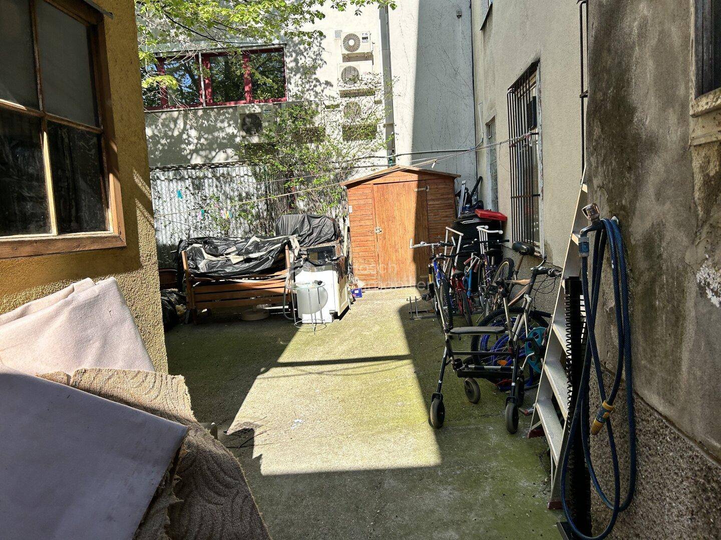 Hinterhof mit einem kleinen Holzschuppen, Fahrrädern und verschiedenen Abstellmöglichkeiten.