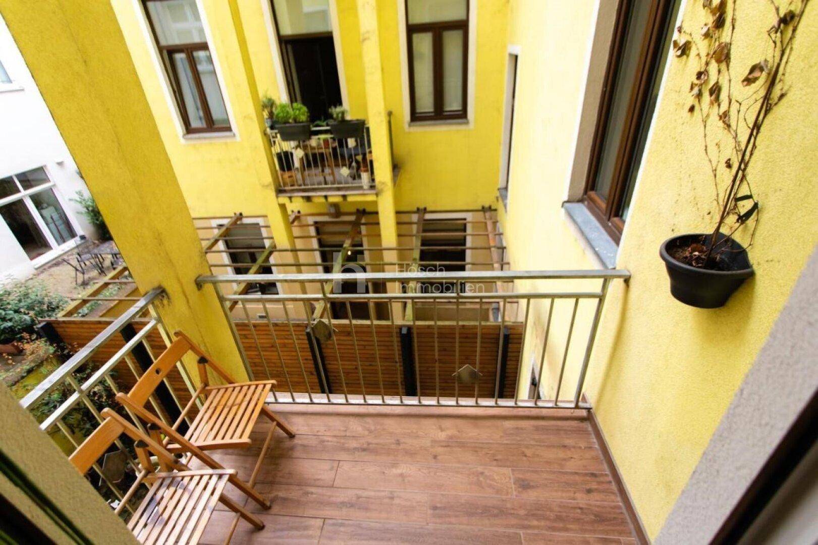 Kleiner Balkon mit Holzboden, zwei Stühlen und Blick in den begrünten Innenhof.