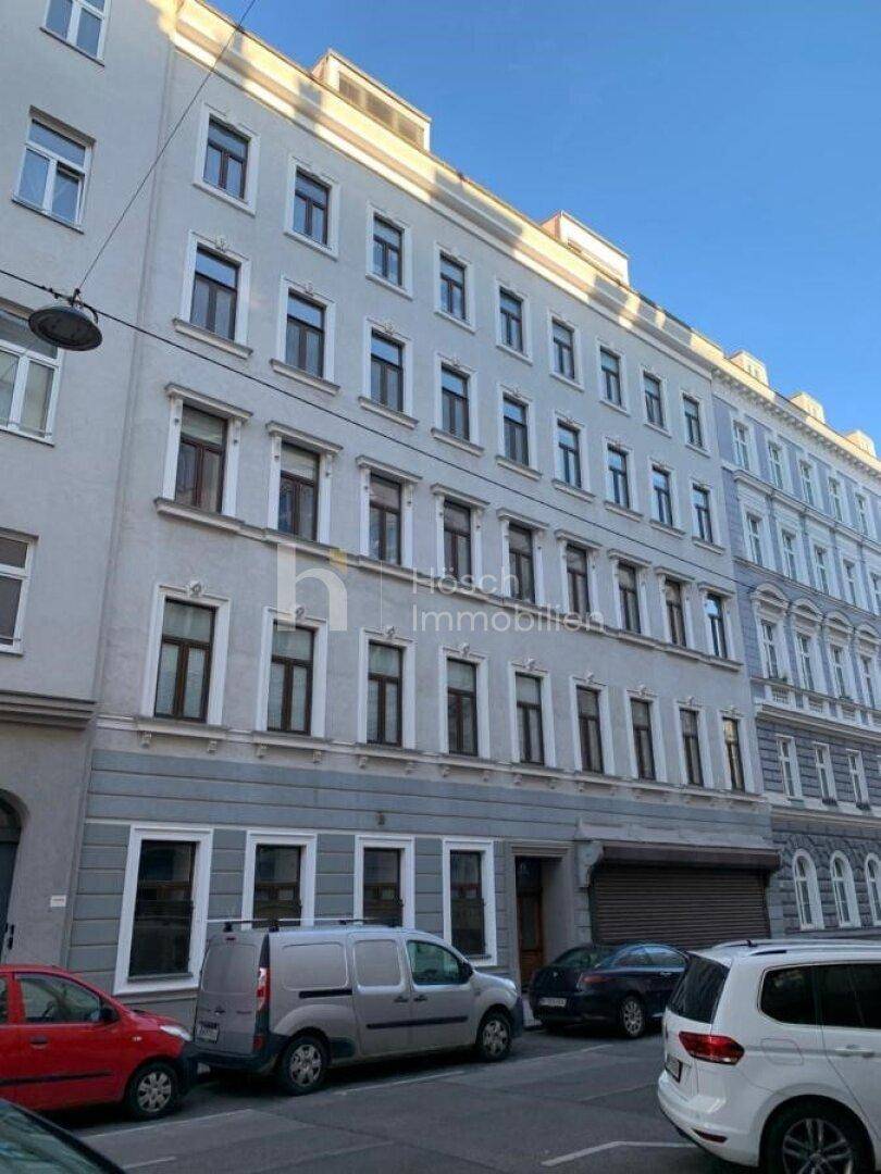 Historisches Mehrfamilienhaus mit klassischer Fassade, vielen Fenstern und parkenden Autos.