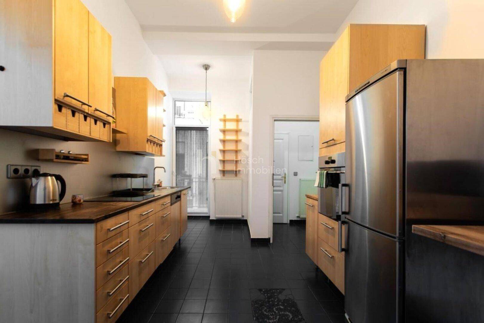 Helle Holzküche mit Edelstahlgeräten, dunklem Fliesenboden und Zugang zum Balkon.
