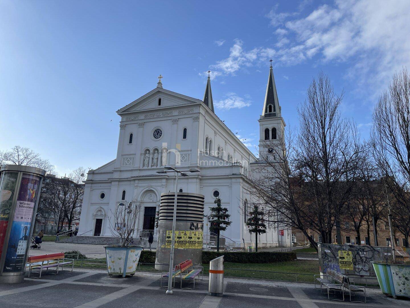 Weiße Kirche mit markanten Türmen auf einem sonnigen Stadtplatz.