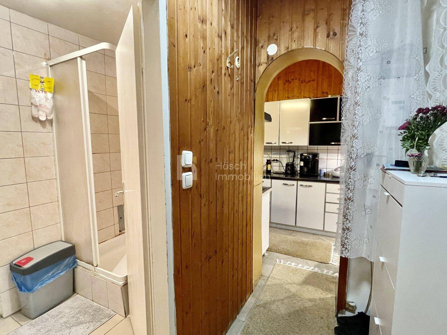 Badezimmer mit Duschkabine und Zugang zu einem weiteren Raum mit Holzvertäfelung.