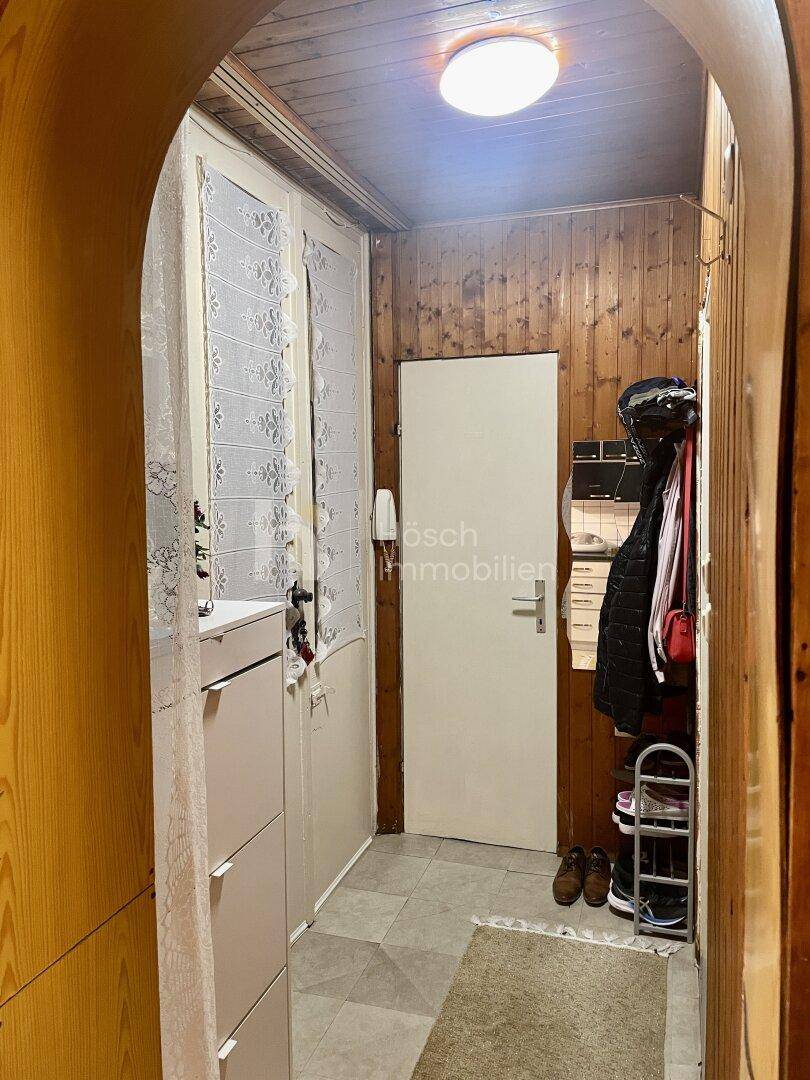 Schmaler Flur mit Holzvertäfelung, Fliesenboden und einem Schuhregal am Eingangsbereich.